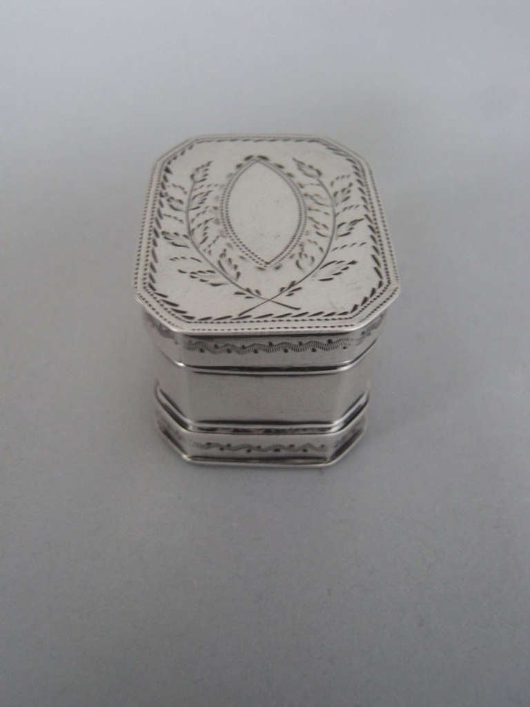 The Nutmeg Grater is broad rectangular in form, with cut corners, and a top and bottom opening. The cover is engraved with a vacant navette shaped cartouche flanked by crossed branches. The sides and base are engraved with wriggle work bands.