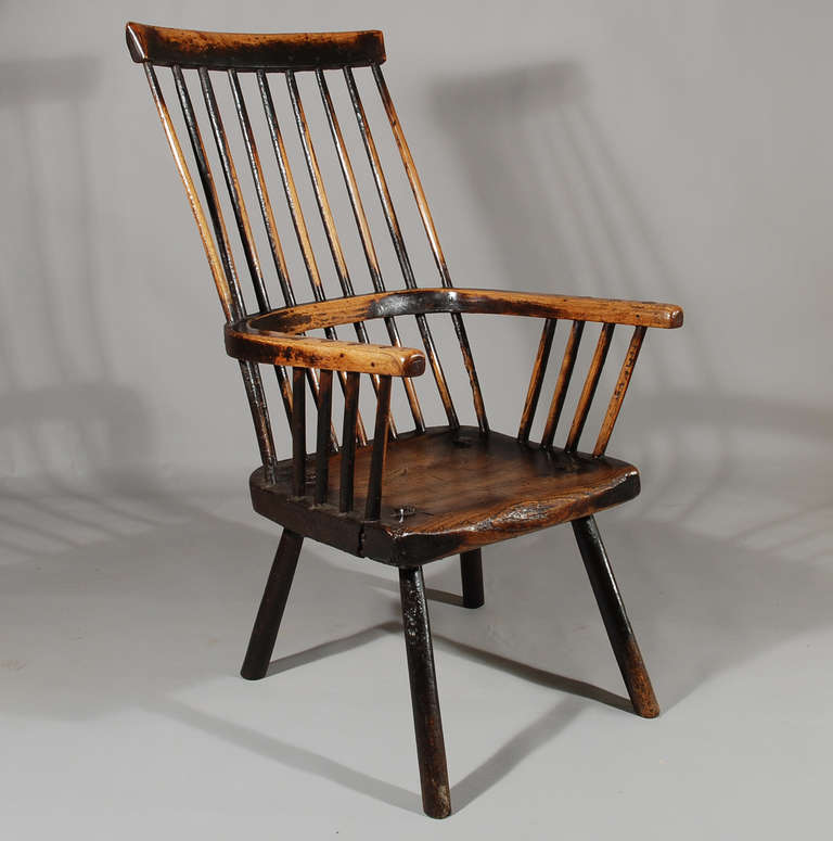 A large and capacious late 18th century primitive Comb Back Windsor chair in ash with chunky seat and single bow arms, the whole raised on turned legs - remnants of old varnish finish.
