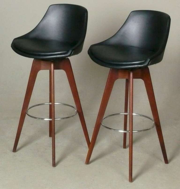 Pair of 1960s walnut and vinyl swivel bar stools with chrome foot rests.  Designed by John Yellen for the I.V. Corp.  New upholstery.