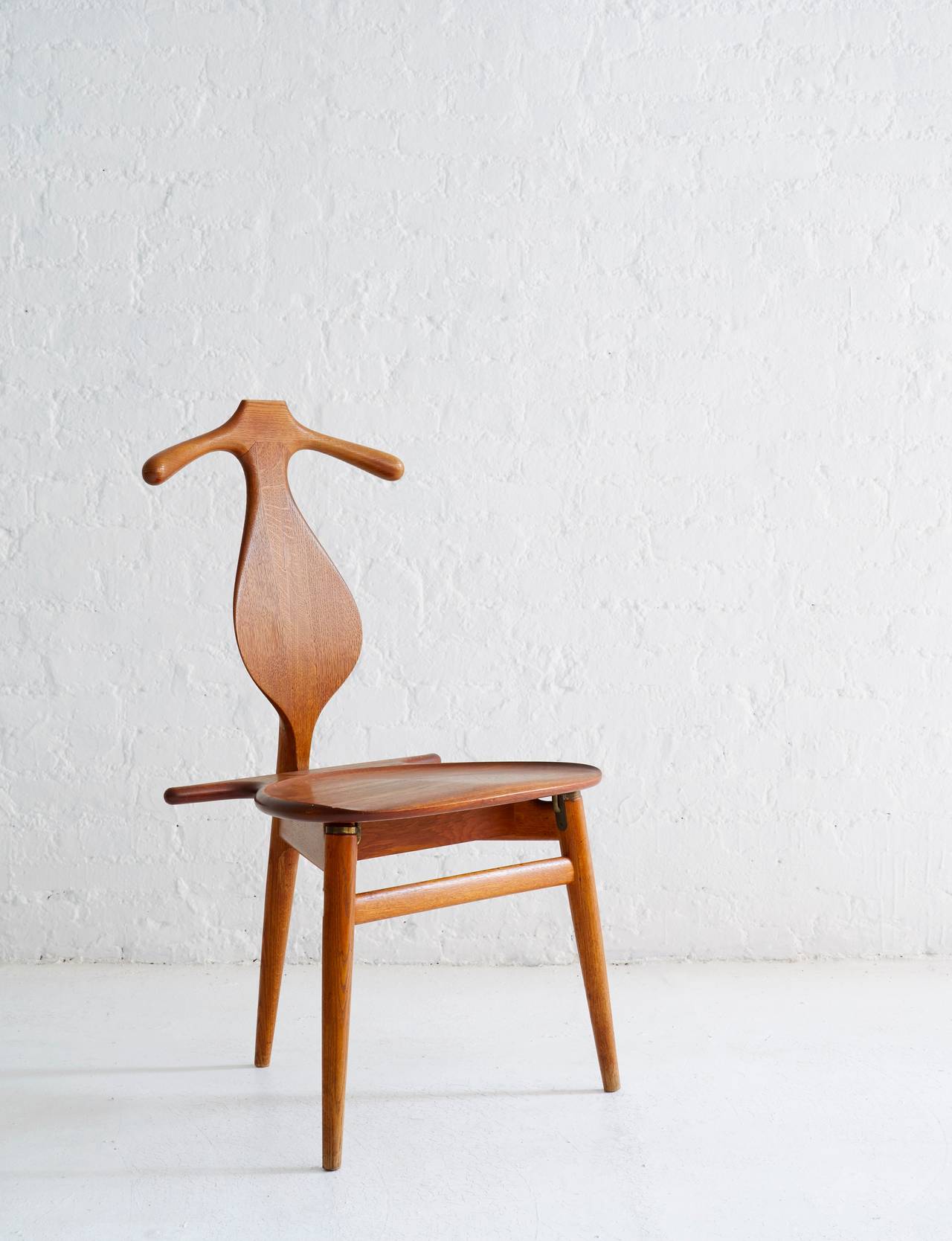 Handsome, iconic Hans Wegner valet chair from Denmark, 1953. 

A functionally designed top rail accommodates a hanging suit jacket, while the seat provides storage. 

Beautiful patina on the oak frame and teak seat. Original brass hardware