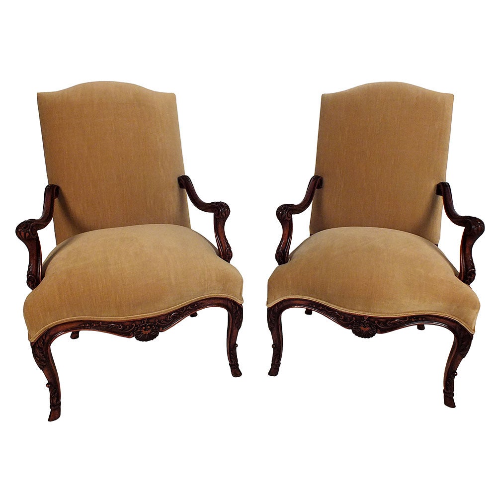 This pair of 1910's French Louis XV-style open armchairs features delicate floral motif carvings on the arms and legs. The chairs have been recently upholstered in a sand velvet fabric with double piping trim. This pair of open armchairs will be a