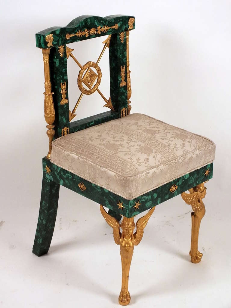 This gorgeous 20th century Empire style chair features a frame made from malachite and bronze. Adorning the carved malachite frame are bronze ormolu accents of arrows, starts, and decorative elements. Standing out from the malachite are the winged