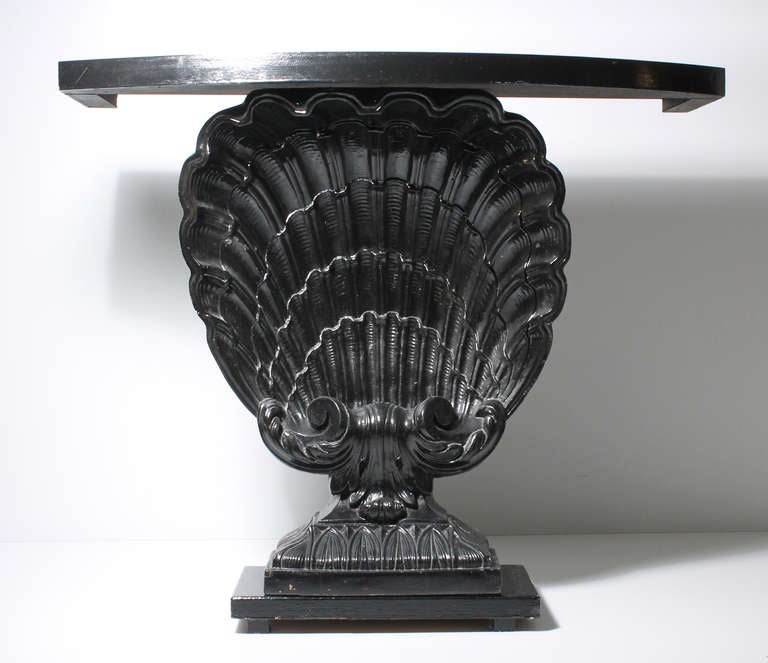 A black Grosfeld House console table with plaster shell motif mounted between wood base and top.