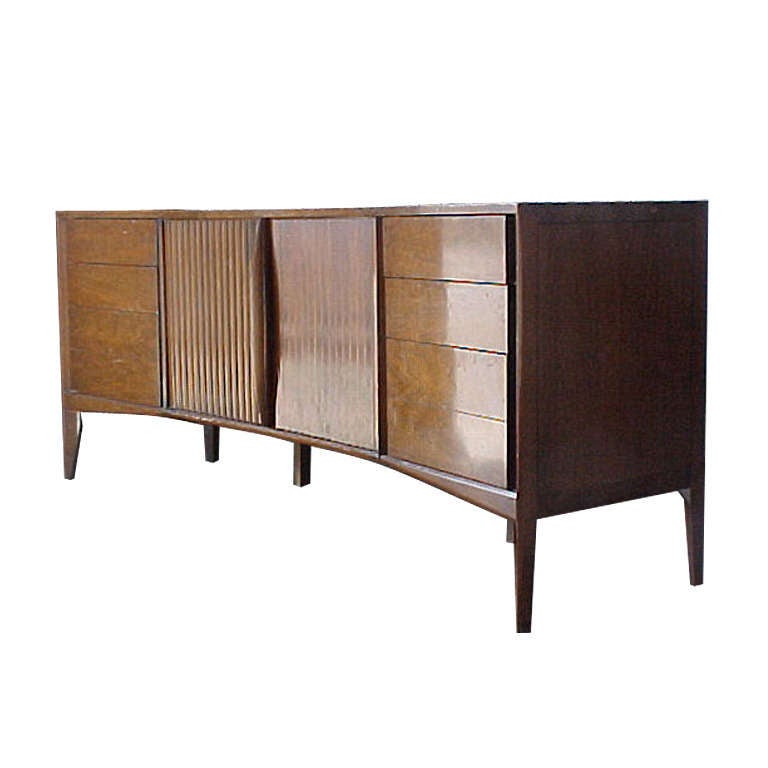 A dramatic sideboard dated 1961. Exceptional quality and craftsmanship. Designed by Hobey and Helen Baker for York County Chair Company. Curved front. Large Faceted doors with beautiful wood grain open to 3 interior drawers. Tapered legs. There were