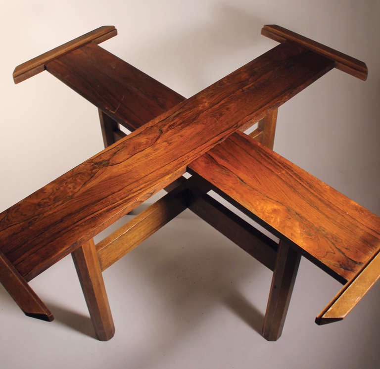 Dynamic dining table with interesting cross form with stretcher wood table base. Looks to be rosewood. Supports a large eight-sided piece of glass that is included. No labels or identifying marks to be certain of a designer, but very much in the