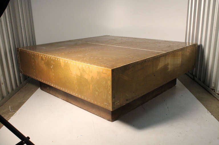 A rare coffee table form by Sarreid. Wrapped in brass with a plinth base. Patinated at this time other than one side where someone cleaned it. The whole table can look shiny but needs polishing. Left as-is at this time in the event someone desires