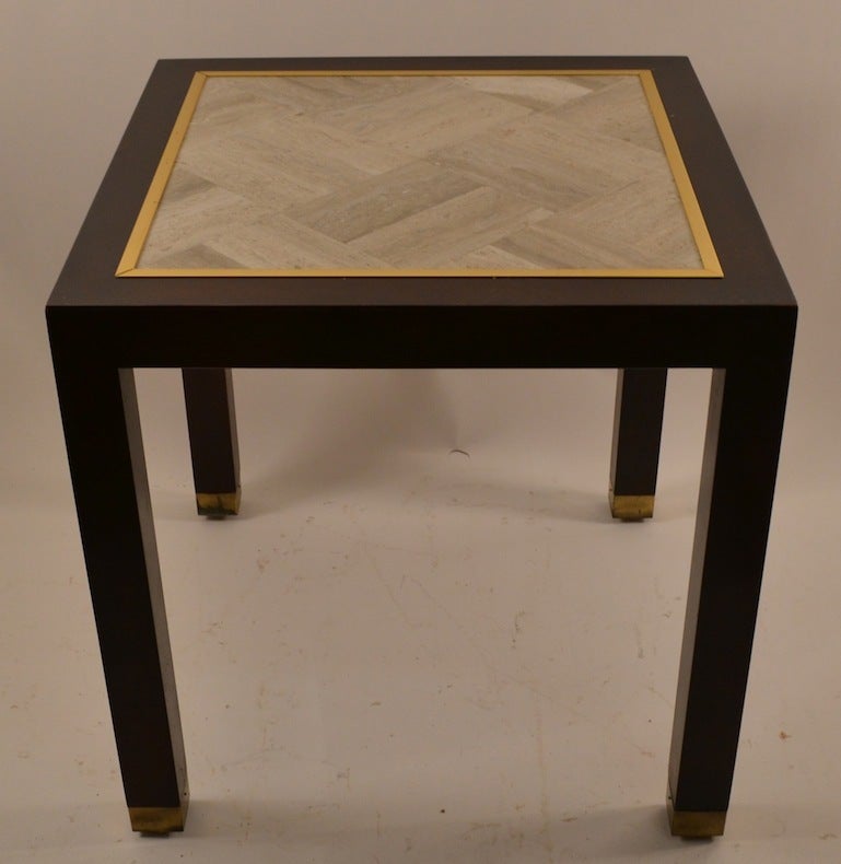 Taylored design square table with parquetry travertine marble top, framed by gold laminate trim, with solid hardwood ( mahogany or walnut ) base, squared legs terminate with brass covered feet. This table shows some minor signs of age and use,