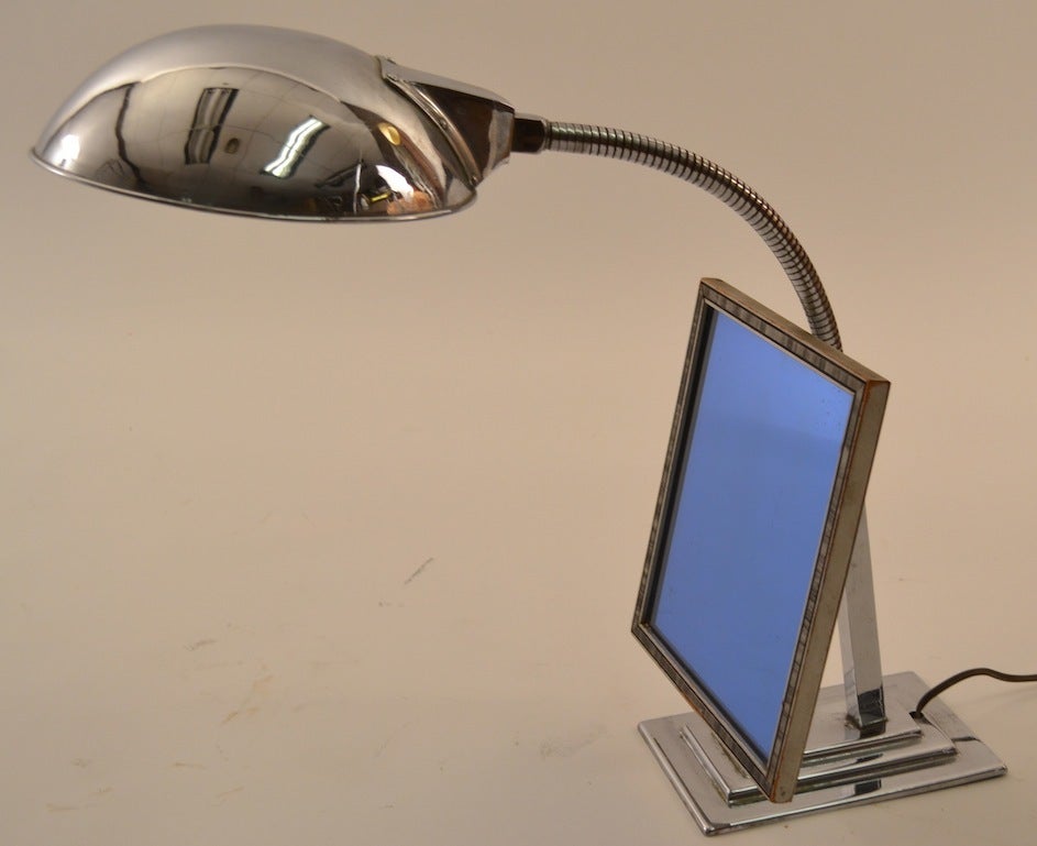 Adjustable chrome lamp with blue glass mirror. The hood shade is on a cable arm, allowing for adjustment of the light, and the mirror also tilts and swivels on a knuckle joint.  American Machine Age make up light, probably originally  from  store