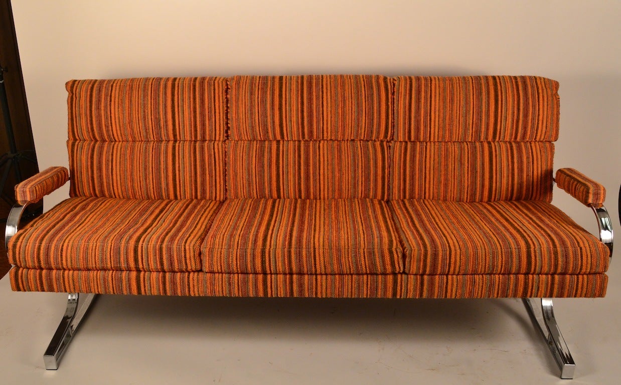 Cool chrome base full size sofa with upholstered seat, back and arm rests. Orange stripped upholstery ( original ) and in good condition. We are also offering the matching chair, and another sofa from this same estate, if you need a large set.