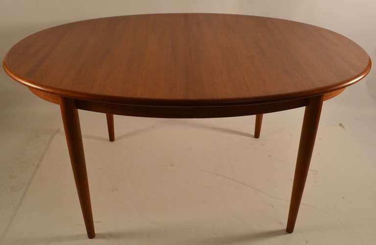 Very clean Danish solid teak table with two large original leaves. Oval table on four conical tapered pole legs. Each leaf 19