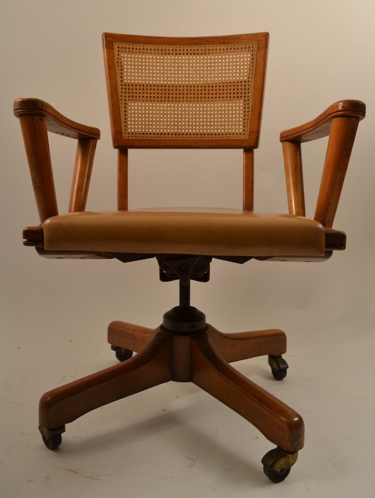 Swivel and tilt desk, office chair. This example has several adjustments including height, back rest angle, and back support tension.  Solid wood frame, caned back rest, and upholstered vinyl seat.