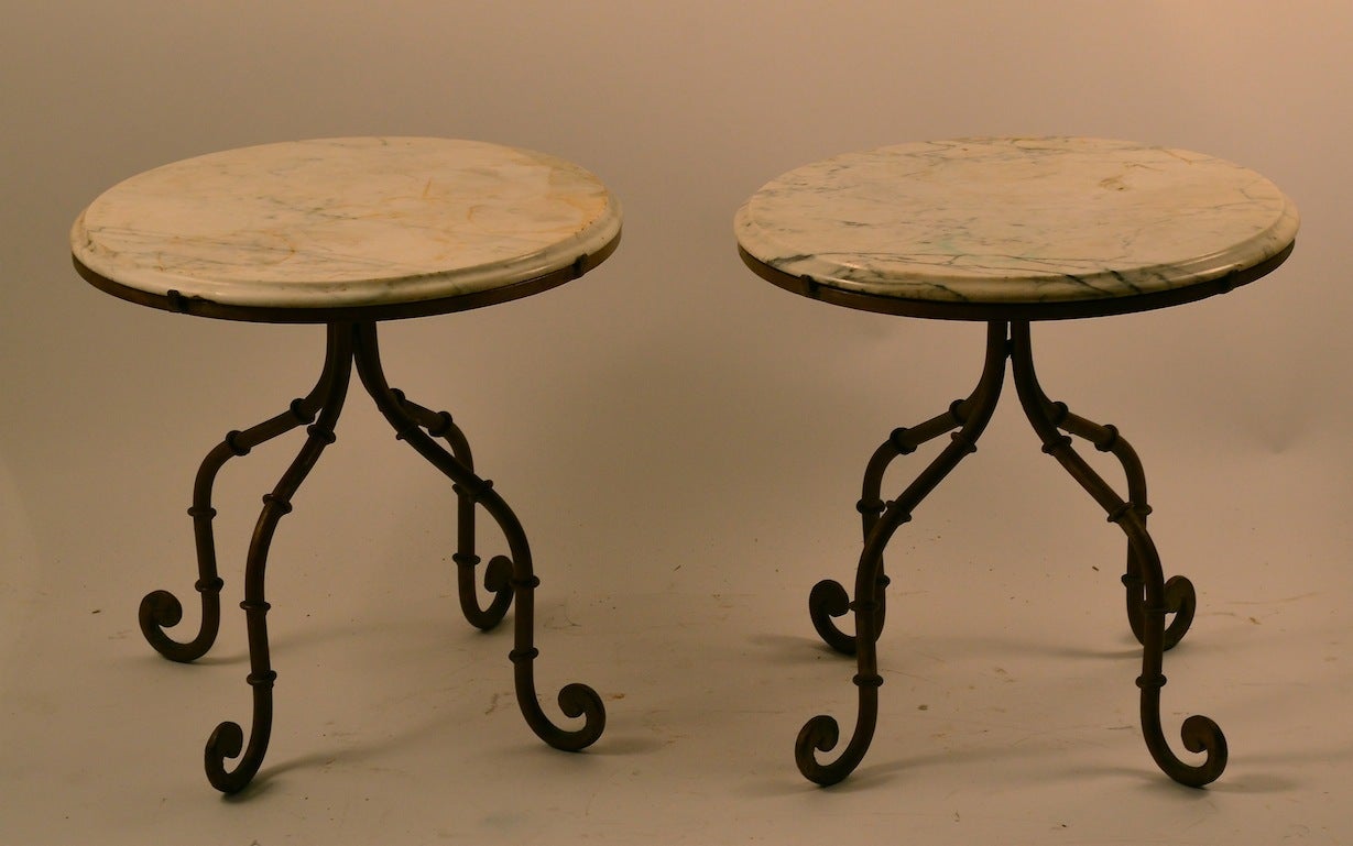 Pair of decorative marble top tables with iron bases, in brass paint finish. The marble tops show some wear and stains, one has a minor chip on the underside, Great for use as plant stands, sunroom, etc or you could replace the marble tops if you