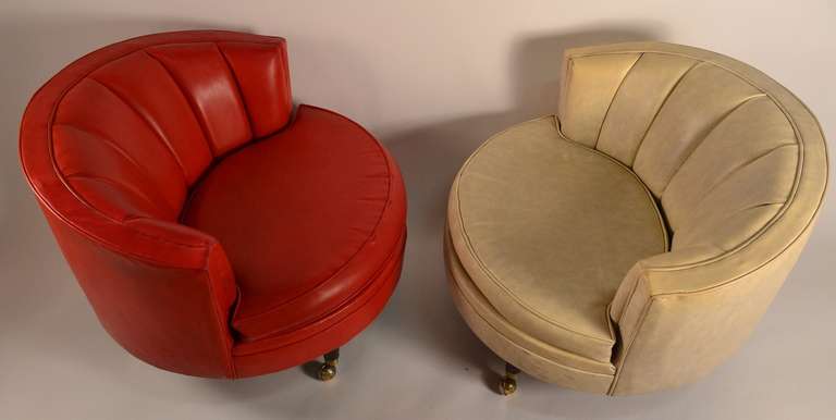 One bright red/orange, one off-white. Both in original vinyl upholstery. Raised on tapered pole legs, with ball form caster feet.