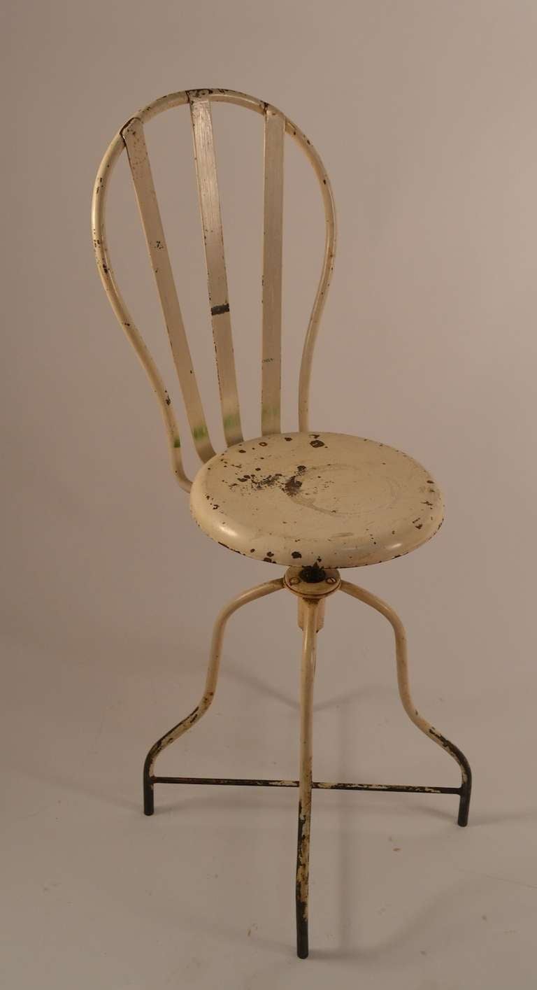 Forme inhabituelle avec support dorsal. Peinture blanche d'origine, usure due à l'âge. La chaise pivote, ce qui permet d'ajuster la hauteur (siège en position haute 23,5