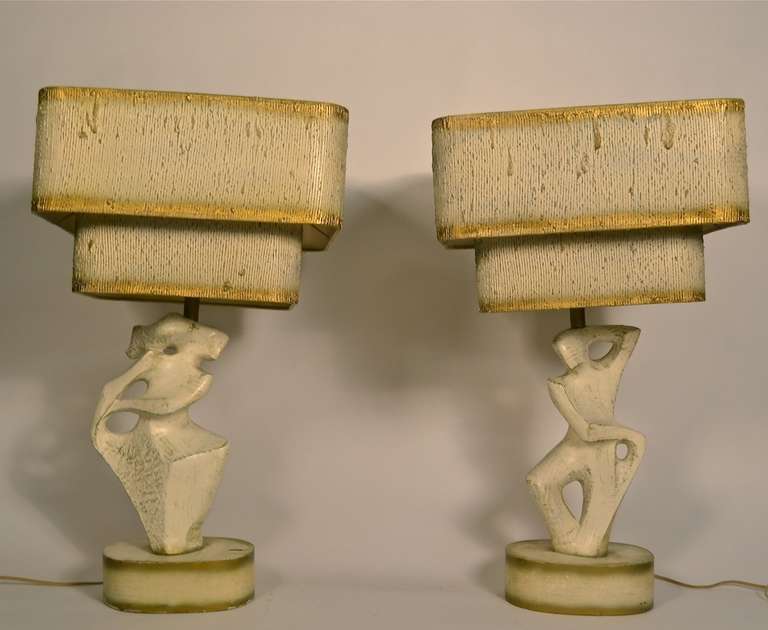 Pair of plaster figural lamps, male and female, with original two tier shades. Off white ground, with gold toning and highlights. Abstract figures mounted on solid wood bases. Classic Mid Century 