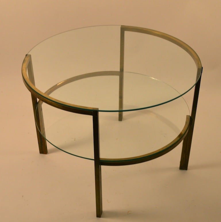 Moderne two tier glass and squared brass table. Round glass top, brass frame  structure and glass second level shelf. Very sophisticated and elegant occasional, end, lamp table.