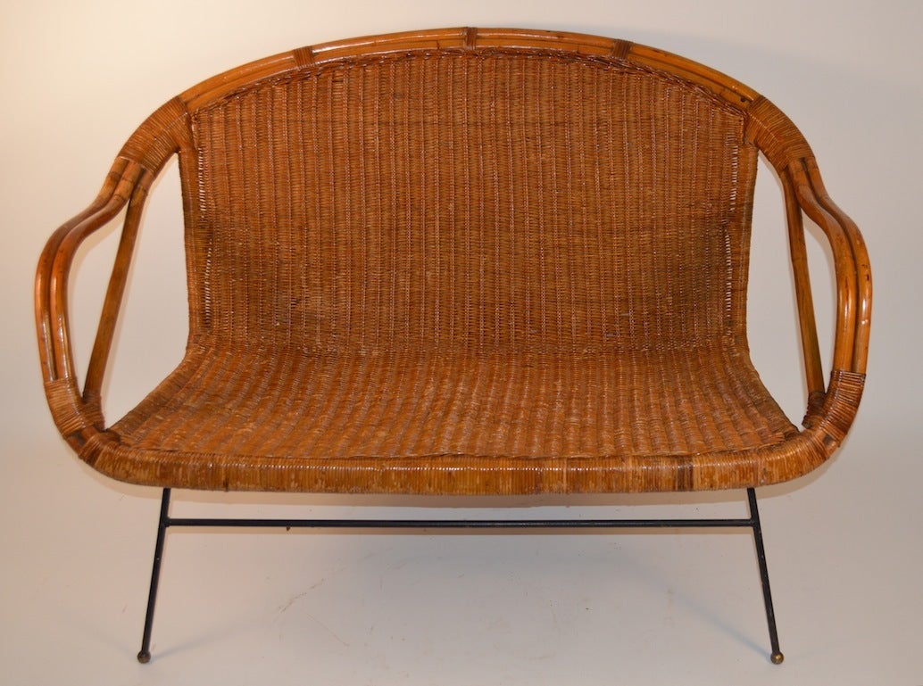 Bamboo frame with woven wicker seat and back, on iron rod legs, with ball feet. Very chic and stylish love seat size settee, probably California made. Great for a screened porch, or casual recreation room.