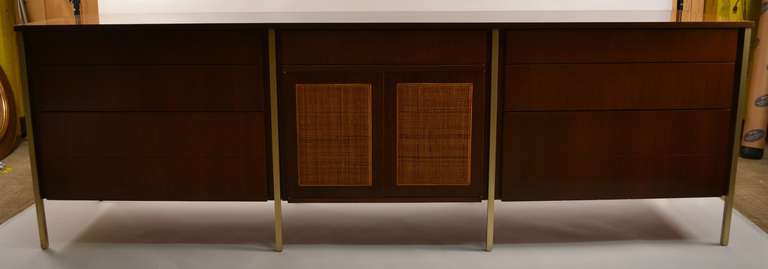 A nice Mid-Century Modern walnut veneer, cane, and metal credenza. The two cane front doors open to a storage space, flanked on either side by a bank of three drawers. Fully marked 