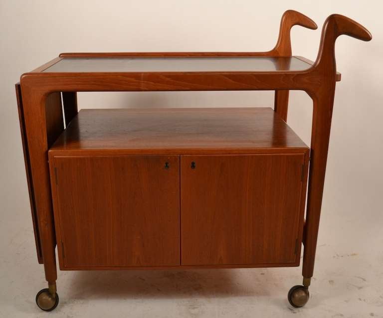 Nice Danish Modern Serving, Tea, Bar Cart. Solid Teal construction features two door storage compartment ( locking with key included ) and a black laminate top work surface. Top has a drop leaf which can be flipped up to create a large (56.5