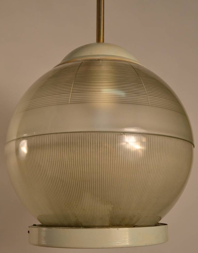 Spherical form Holophane shade hangs from brass tube. Capable of high wattage generating high light if desired. Metal cap, and ring at top and bottom