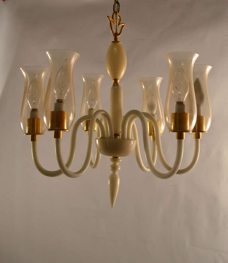 Elegant six arm uplight fixture, each arm supports a candle bulb, surrounded by a hurricane shade. The body of the fixture is cream glass with gold flake inclusion, while the shades are clear glass with gold flake inclusion. 
Italian Murano Art