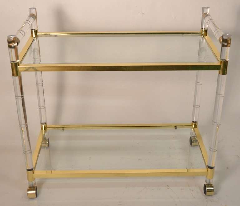 Very nice example of the work of CHJ - bevelled glass shelves ( minor scratches  to surface of shelves ) two tier serving /bar cart. The lucite, and brass surfaces are in extra fine condition, and the wheels roll freely.
