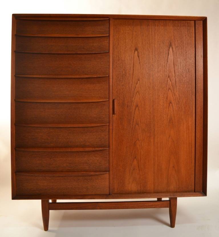 Teak chifferobe, seven drawers on one side, a tambour door door on the other side, which opens to reveal nine interior storage drawers. Original finish, and condition, some minor wear to finish.