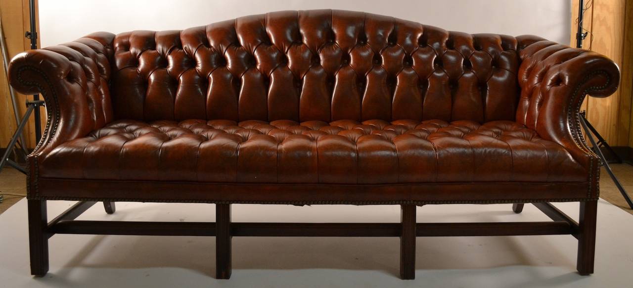 Vintage 1970's example of classic English  Camel Back form sofa. Fully button tufted back, arms, and seat, brass stud trim, solid mahogany stretcher base.  Very fine original condition, very slight chip on base of front leg, as shown. Bears label