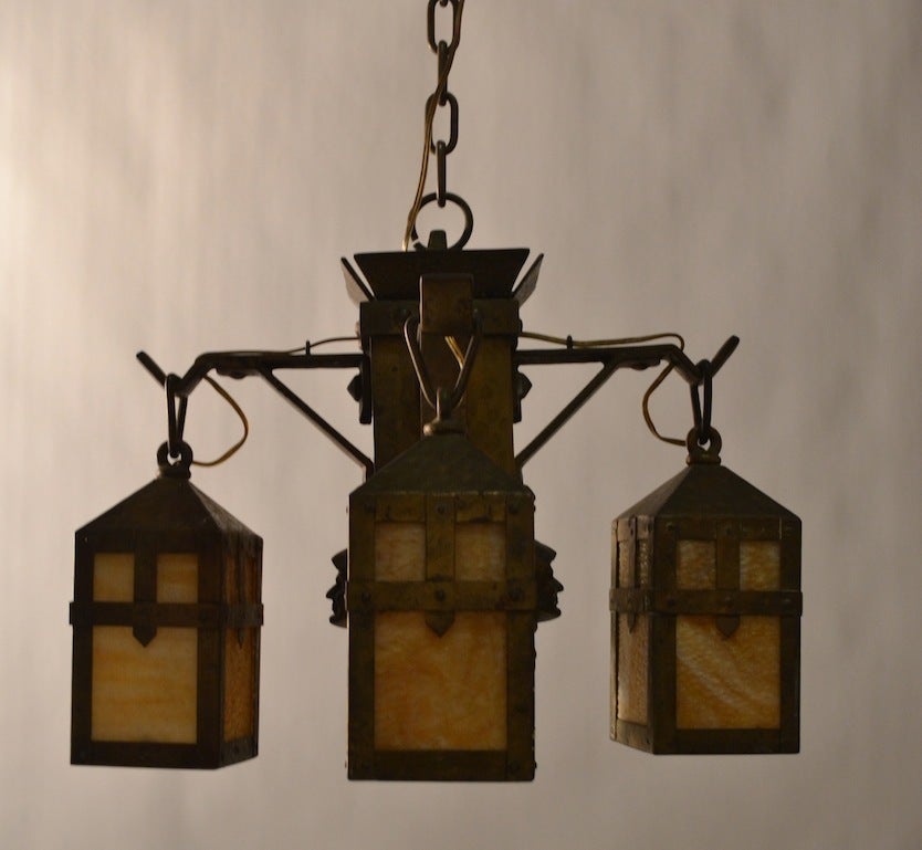 Four lanterns hang from the center post, each lantern has its original slag glass. The four sided center has a Monks face looking outward. This clssic Arts & Crafts, Mission, Gothic Revival fixture was produced by the well respected and highly