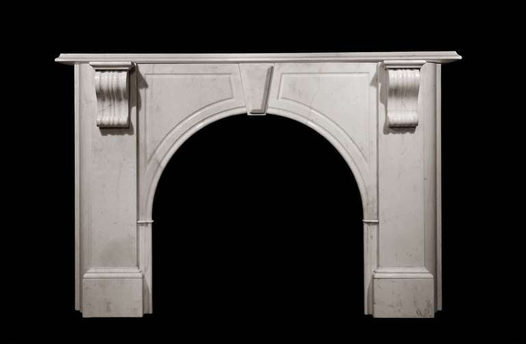 A Carrara marble arch mantel having scroll corbel supports, simple fielded panels and key stone. Opening dimensions: 38.25