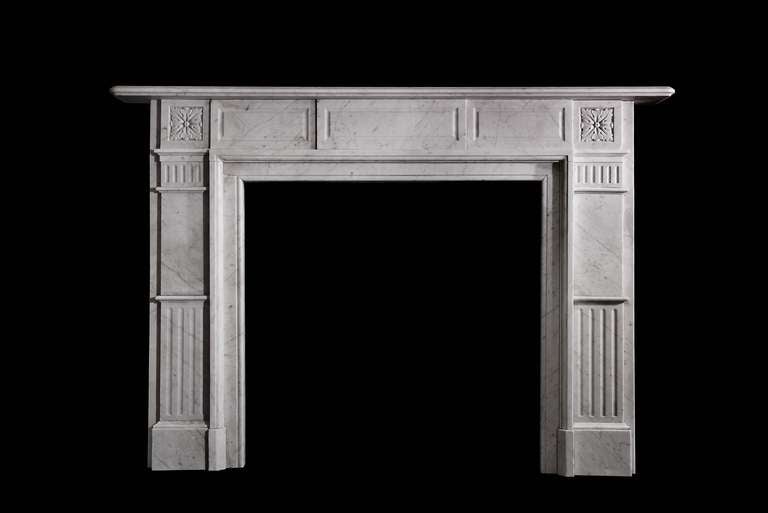 Carrara marble Edwardian mantel with fluting along the jambs, fielded panel across the frieze and carved rosettes on the corner block. Opening dimensions: 38