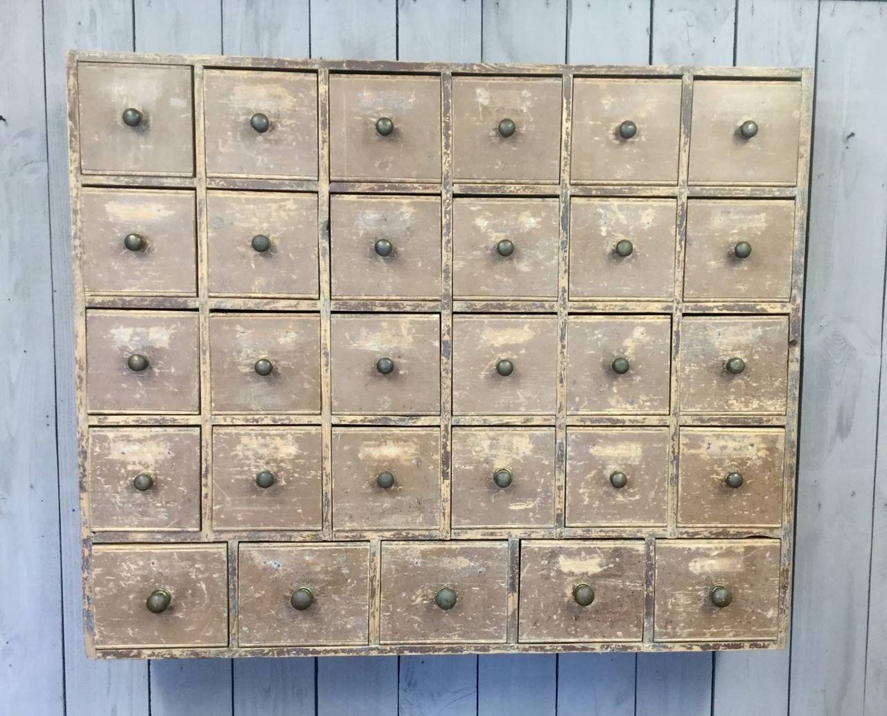 An original wall-mounted cabinet from an English seed merchant's shop.  This cabinet is in excellent condition and has been hand-scraped to reveal the original paint.  It features 29 drawers with the original brass pulls.  This is a fabulous