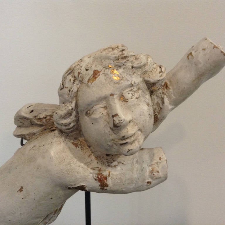 A charming French cherub fragment from the Baroque period.  The cherub was once gilded.  Now, stripped of the gild and bole to review the creamy white gesso with traces of the gild remaining.   It is mounted on a bespoke iron base.  It would make a