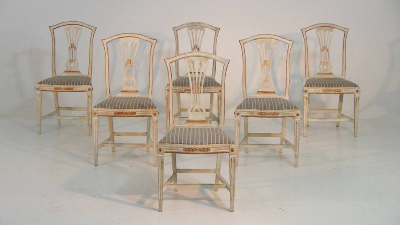 A stunning set of six Gustavian style dining chairs in original paint and gold gilt.  The paint color is ivory with gilt detailing and traces of the original red bole peeking through in areas.  

There are a total of 5 moldings missing from 3 of