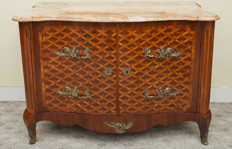 An unusual Louis XV style walnut and fruitwood parquetry two-door commode. The front and sides are inlaid with geometric parquetry. The commode has a serpentine pink marble top over a conforming case that is raised on cabriole legs and ends with