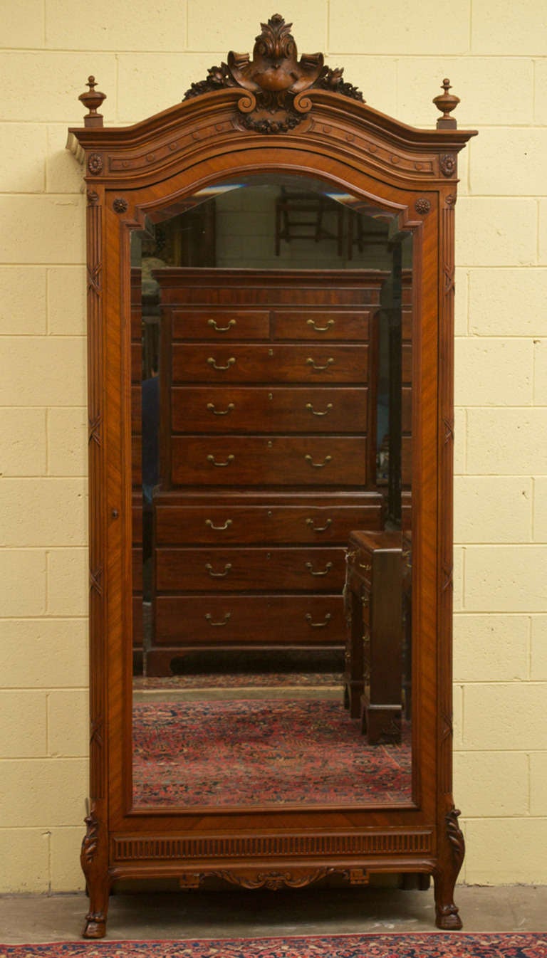 A gorgeous Louis XV Style walnut Bonnetiere with a beveled glass mirror single door.  The carved, arched crown is flanked by finials.  The door is above a lovely carved apron that sits on cabriole legs ending on hoof feet 