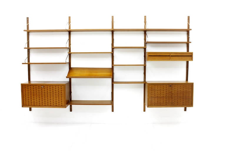 Nice teak wood wall system by Poul Cadovius in a rare version with brass holder.

2 x Cabinet with one door
1 x Cabinet with two drawers
1 x Magazine / book holder
6 x Shelves 80 x 20 cm, 
2 x Shelves 80 x 30 cm,
4 x Shelves 60 x 20 cm
5 x