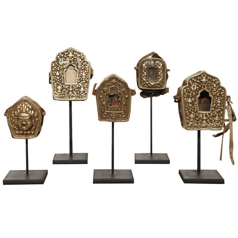 A collection of traveling shrines from Tibet circa 1850. Each has a brass front and copper back panel. Most also feature a leather cord. Also known as a Gao, these shrines were worn as jewelry and usually held a written prayer.

Left to right:
