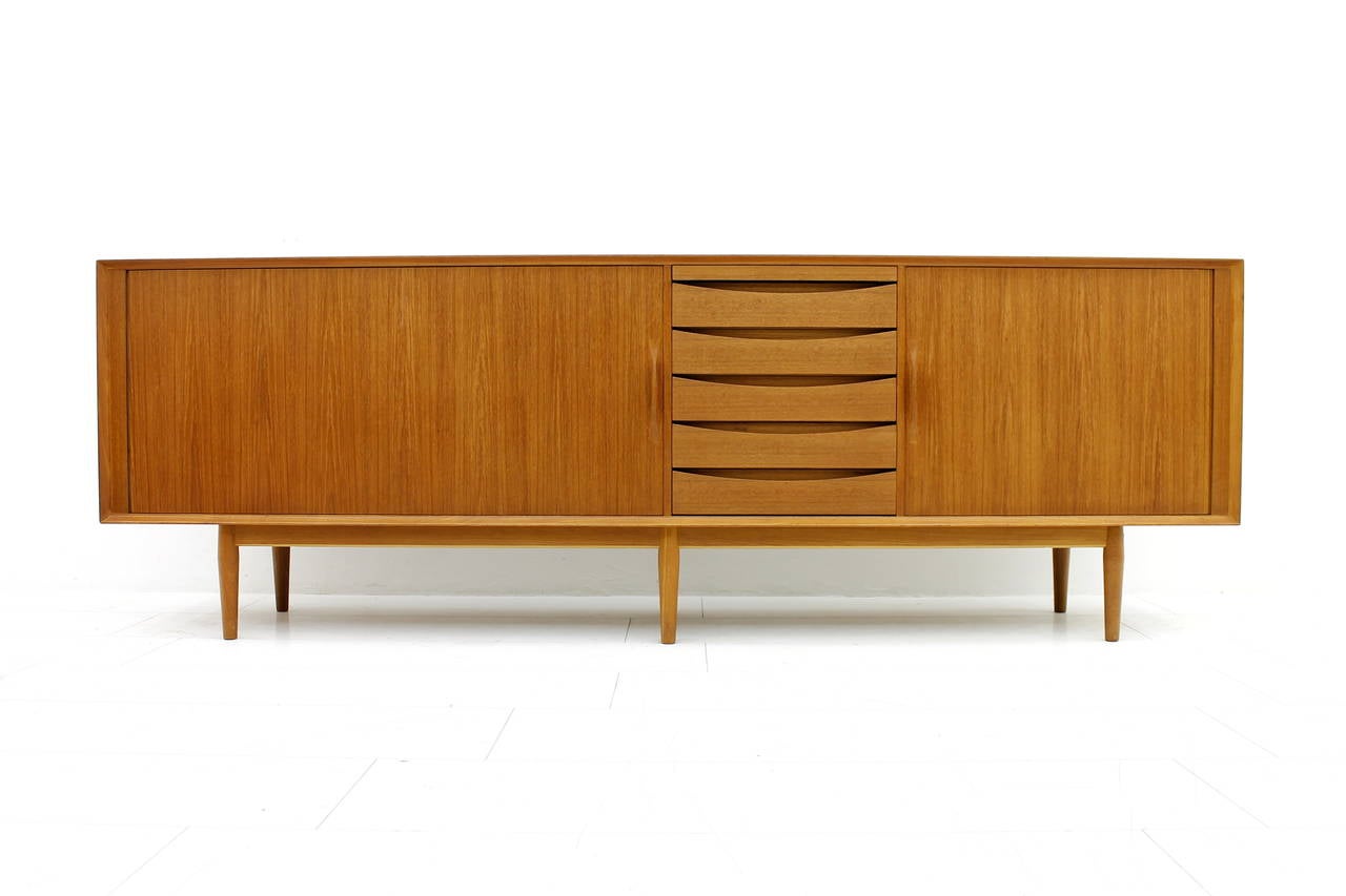 Teakwood sideboard designed by Arne Vodder and made by Sibast, Denmark model 76. Two tambour doors, five drawers and one leather tray to pull-out.

Measures: W 250 cm, D 50 cm, H 84 cm.

Excellent condition !

Worldwide shipping.