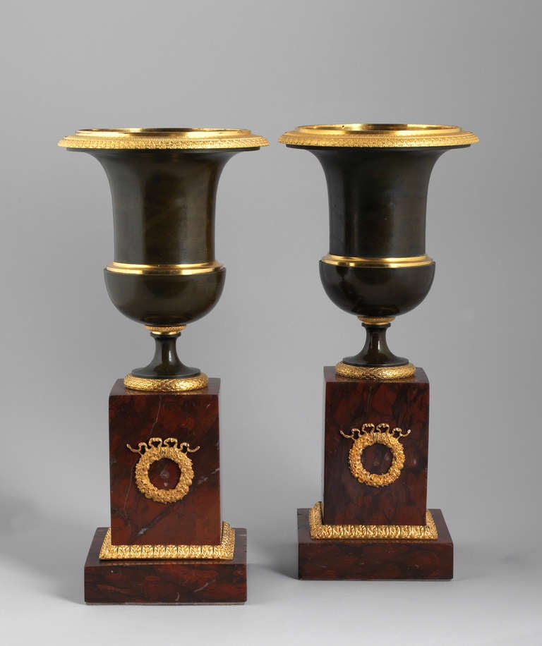 Antiqe crater-shaped patinated bronze vases, mounted on square based red marble plinths. The rims are decorated with delicately crafted ormolu flowers and classizist elements. The vase-bases adorned with ormolu laurel wreaths the marble plinth with