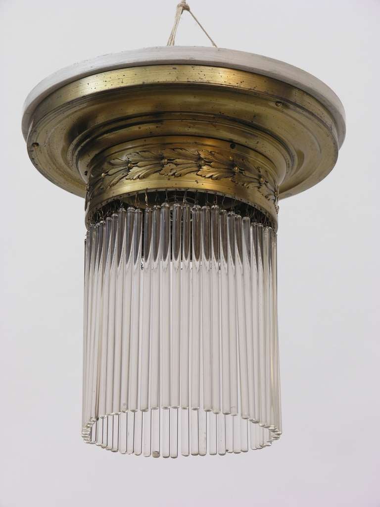 This brass lamp with floral decoration and glass rods is fixed to the ceiling.