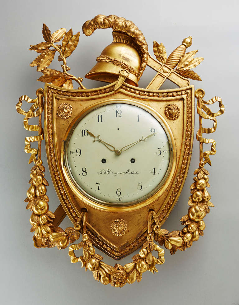 Fine and rare Empire Swedish cartel clock. Very elaborately carved wooden case in the form of a trophy with a shield, helmet, sword and laurel leaves. The dial signed J.F. Cedergren Stockholm (Johan Fredrik Cedergren, 1774-1839). Very good, original