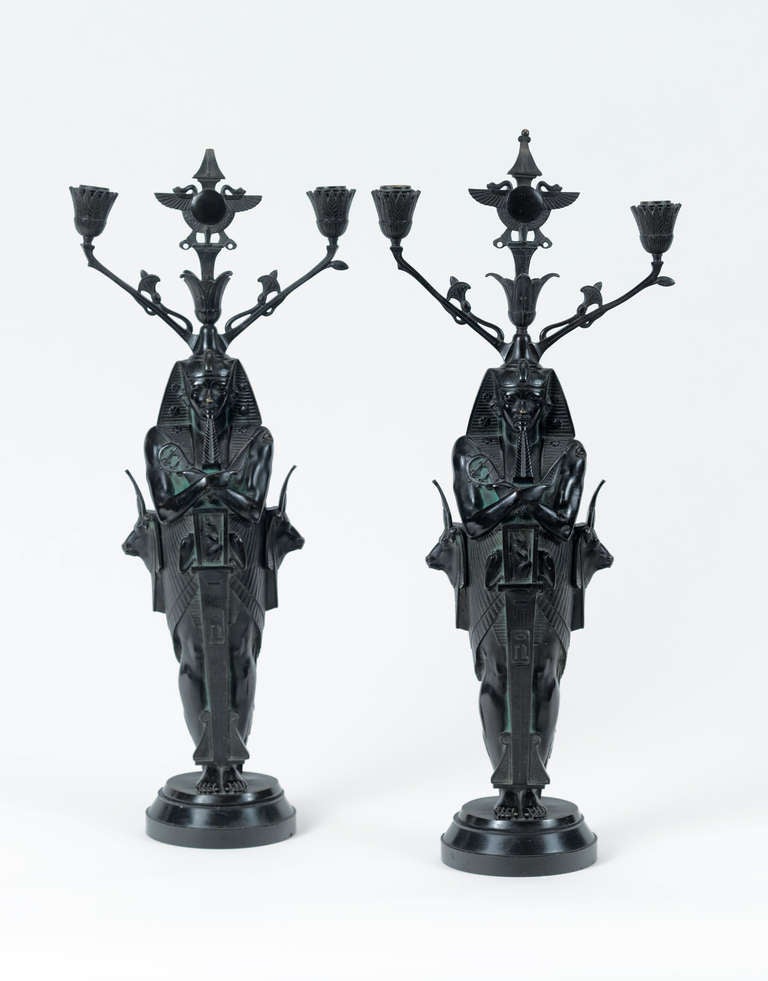 A very decorative pair of egyptian revival patinated bronze candelabra, modelled as a pharoah supporting the central egyptian symbol of Re, a sun disk, laterally two arms decorated with stylized lotus leaves, supporting cone-shaped nozzles, the back