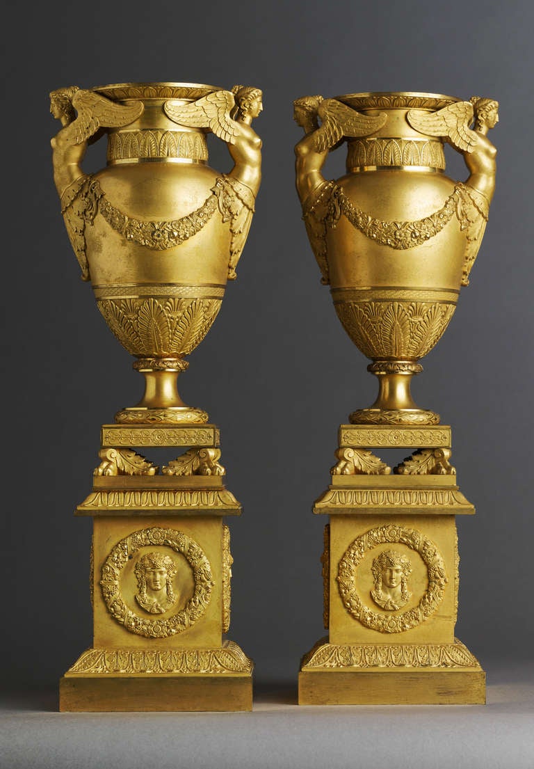 A superb pair of Empire gilt bronze vases, each of krater form with grotesque figurines as handles, on a square plinth with pawn feet. The body with finely chased decor of palmettes and garlands, raised on an architectural pedestal, of which each