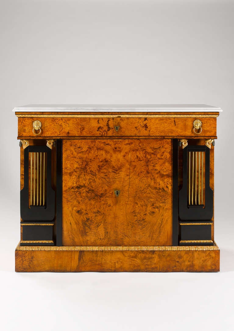 This rare and unusual side cabinet displays very characteristically the elegance of Viennese Empire furniture from the early 19th century. The white marble-top above a long single drawer in the frieze. The door, flanked by two ebonized lyres with