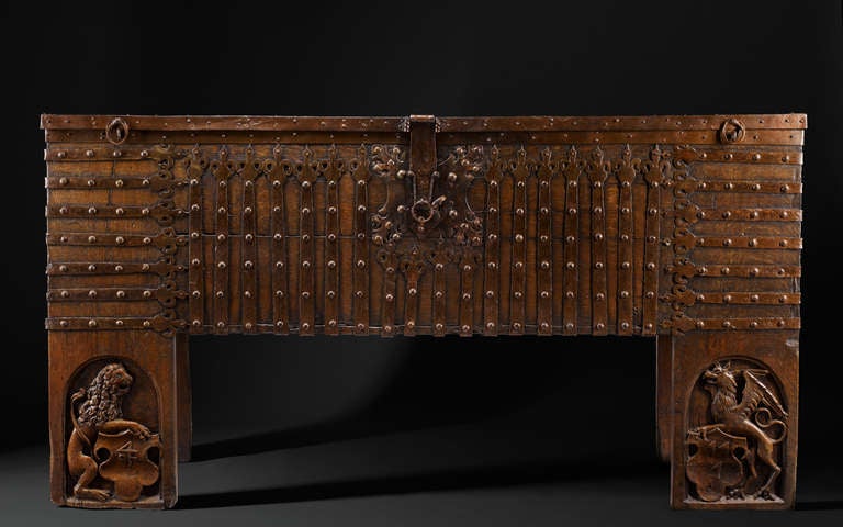 Rectangular standing chest with full-height stiles, extensively mounted with long ironwork straps with trefoil finials which ’wrap’ around the chest edges. These are fixed with convex head nails: running vertically up the front eighteen straps;