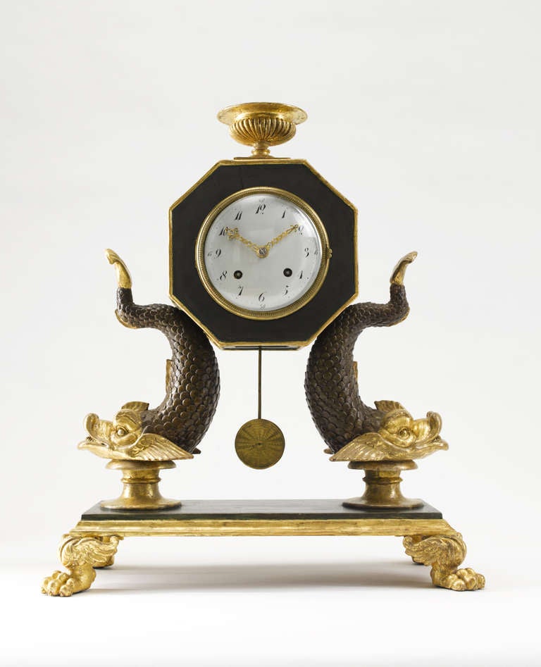 The octagonal shaped case surmounted by a classical vase on dolphin supports, white enamel dial, eight-day going clock movement striking the half- and full hours.