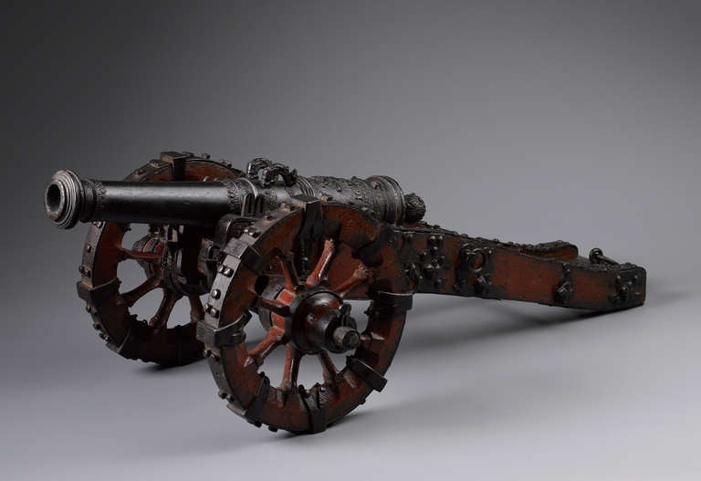 An extraordinary fine and rare model cannon, dated 1671, the barrel cast in bronze and mounted on a wooden carriage. The iron fittings are forged in the minutest details and correspond to the skilful chiselling of the barrel that shows two dolphin