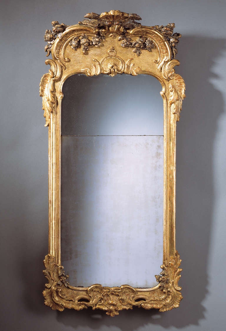 The slightly-arched rectangular divided plate within a moulded framed, the pierced apron carved with a shell, scrolls, flowers and two wings, surmounted by a conformingly decorated pierced arch-shaped cresting centred by two silvered billing birds