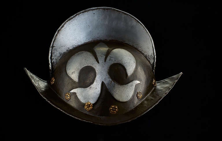 The skull is forged in two halfs, joined at the edge of the high comb. On both sides there is an embossed Fleur de Lys, left blank like the high comb and silhouetting against the blackened ground of the skull. For the attachment of the lining there